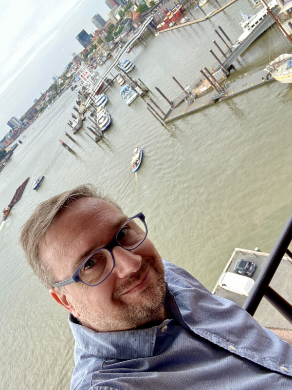 Selfie von André von der Aussichtsplattform der Elbphilharmonie. Im Hintergrund die Elbe und die Landungsbrücken.