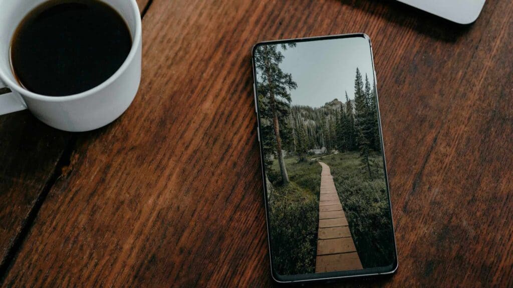 Ein Smartphone mit einem Bild einer ruhigen Waldlandschaft, auf einem Tisch neben einer Tasse Kaffee