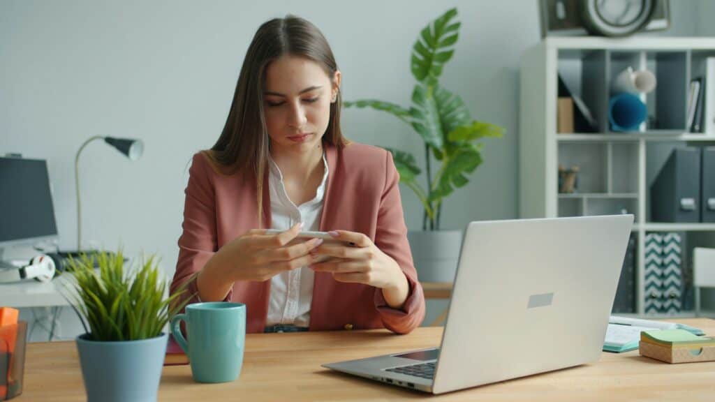 Eine Person sitzt gedankenverloren am Schreibtisch vor dem Computer und spielt mit einem Stück Papier – Prokrastination überwinden